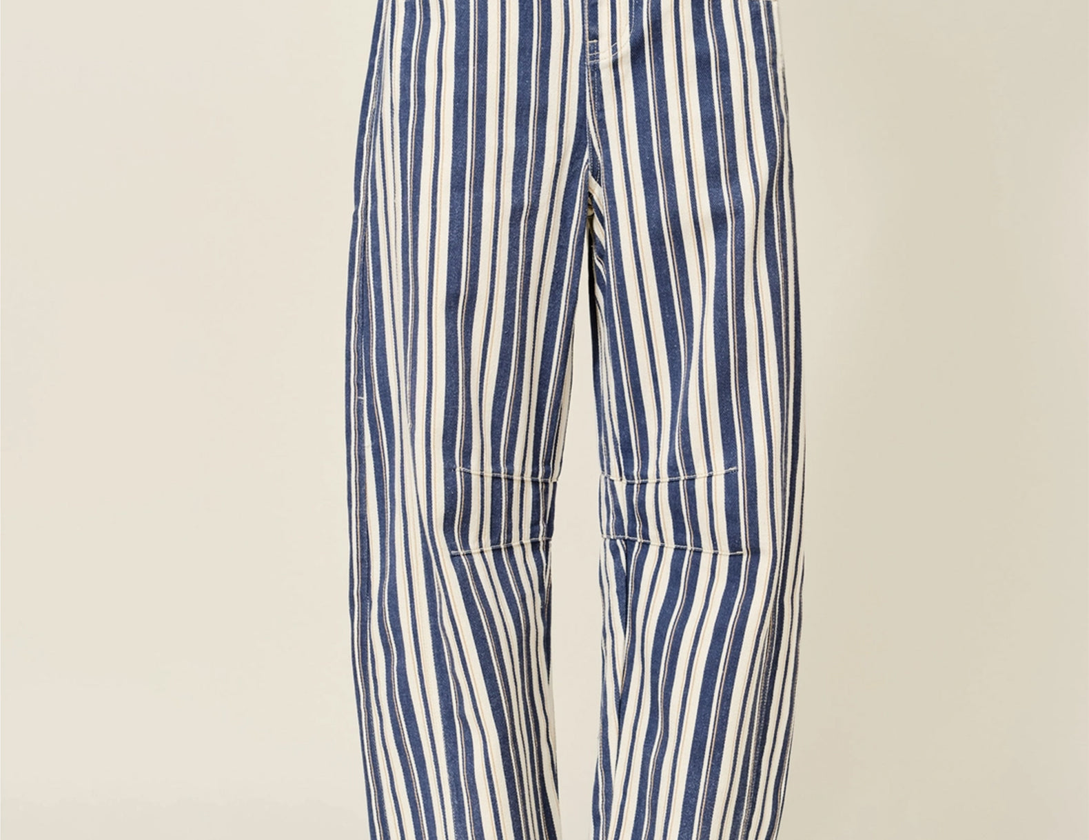 A person wearing loose, wide-leg striped pants with vertical blue and off-white stripes, paired with brown lace-up shoes, photographed against a plain light beige studio background.