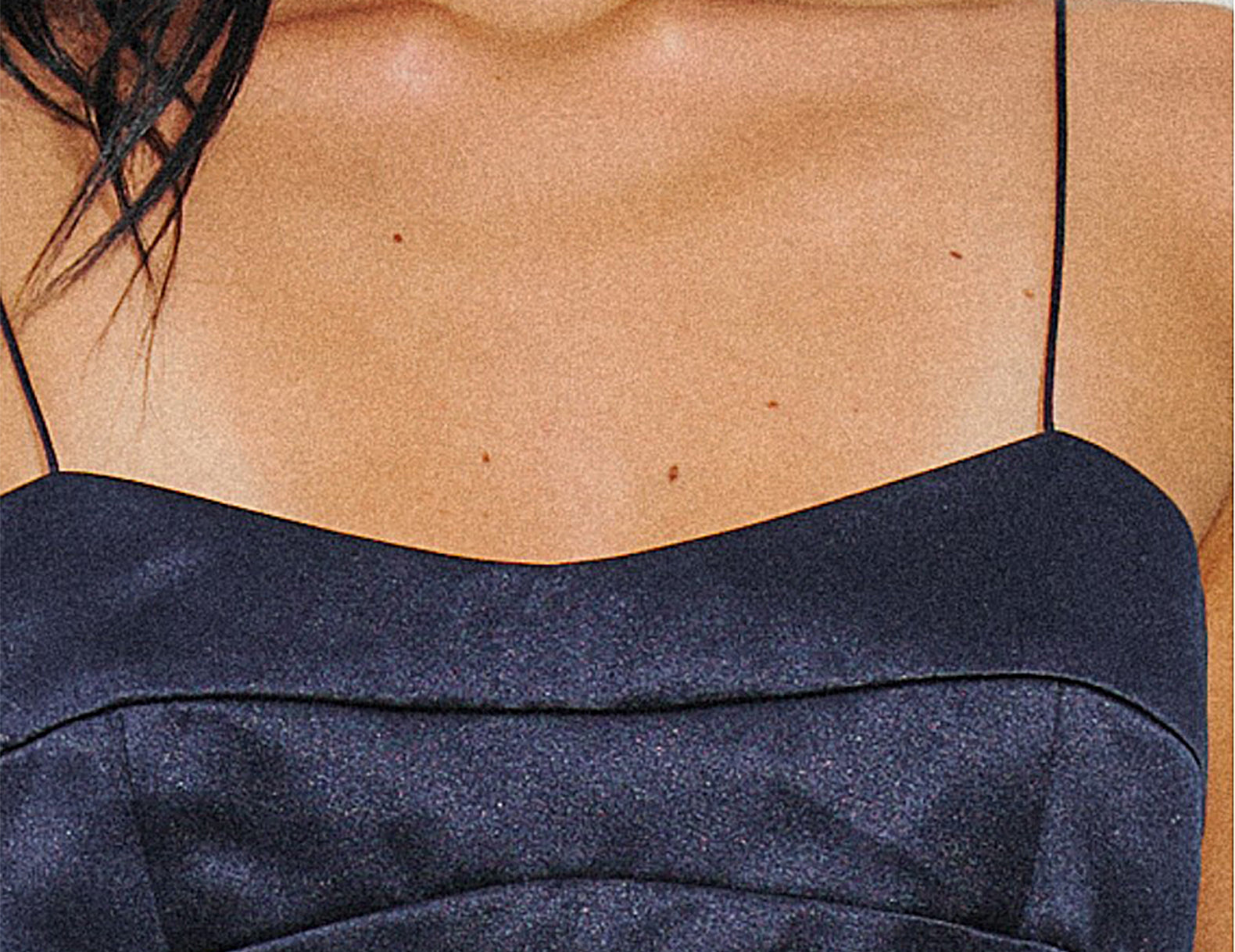 Close-up of a model wearing a dark navy satin spaghetti-strap top, showing the chest, neck, and shoulder area.