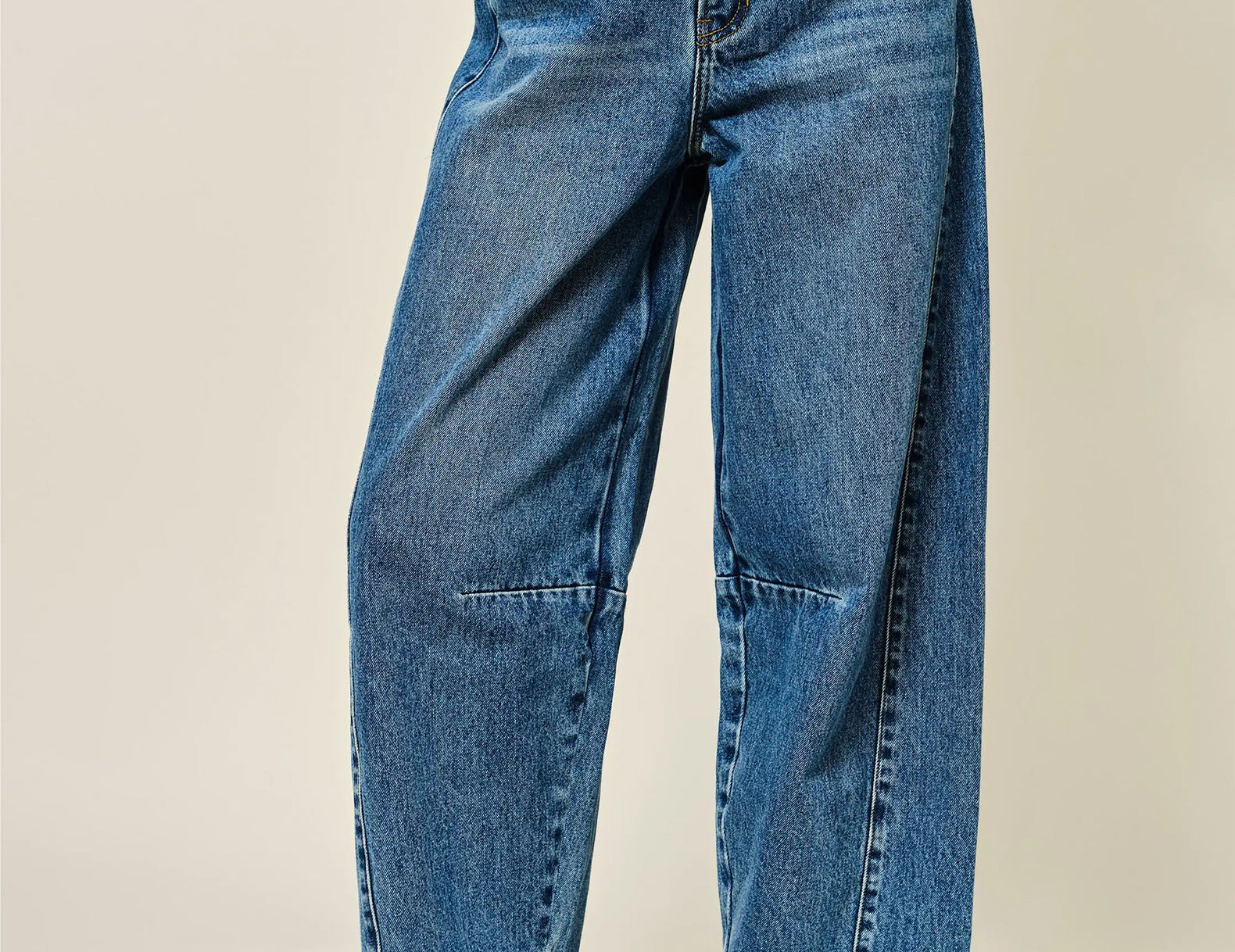 A person wearing high-waisted, wide-leg blue denim jeans with brown leather loafers, shown from the waist down against a plain beige studio background.