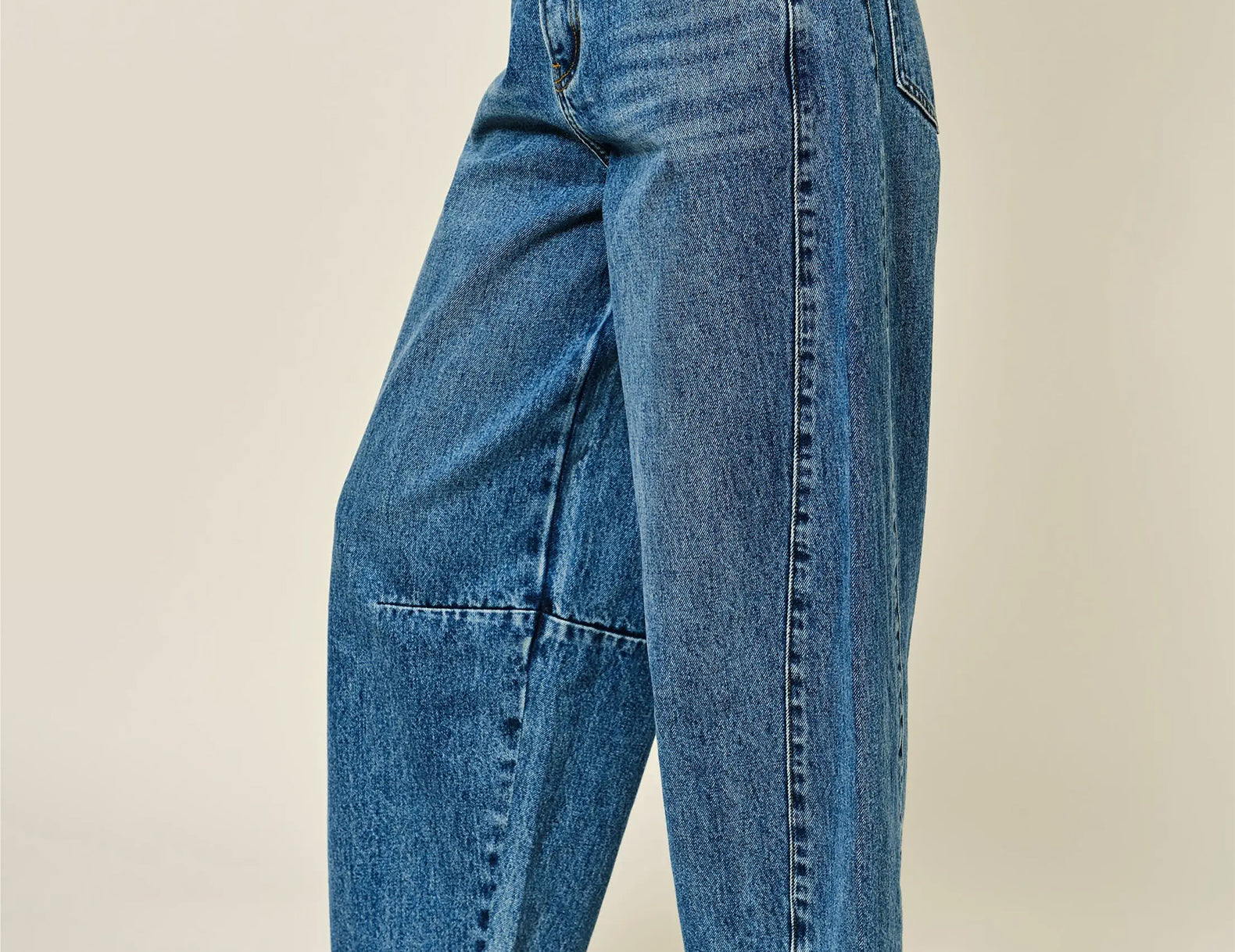A person wearing high-waisted, wide-leg blue denim jeans with brown leather loafers, shown from the waist down against a plain beige studio background.