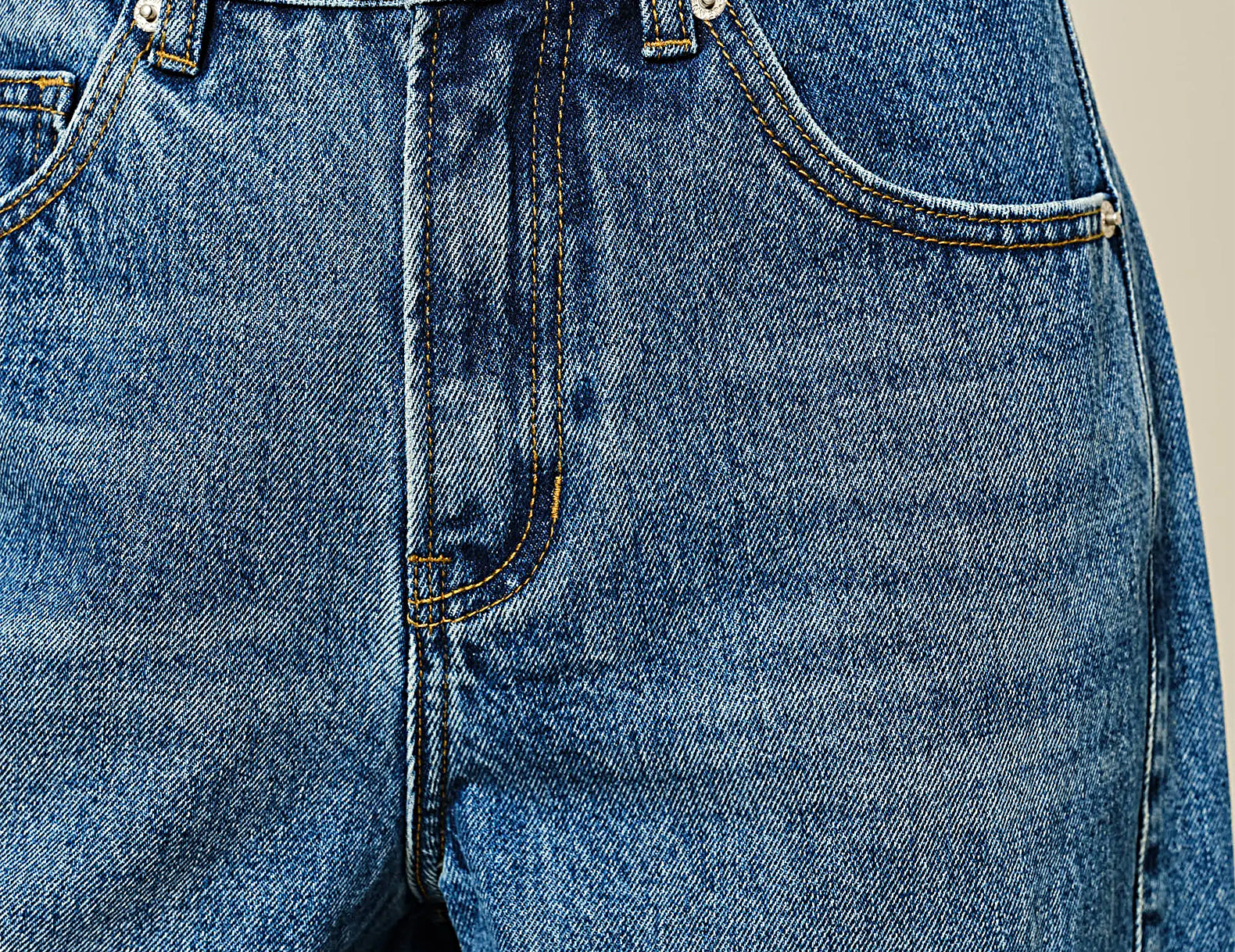 Close-up of a person wearing blue denim jeans, showing the front waistband, button, belt loops, pocket edges, and denim texture against a plain light background.