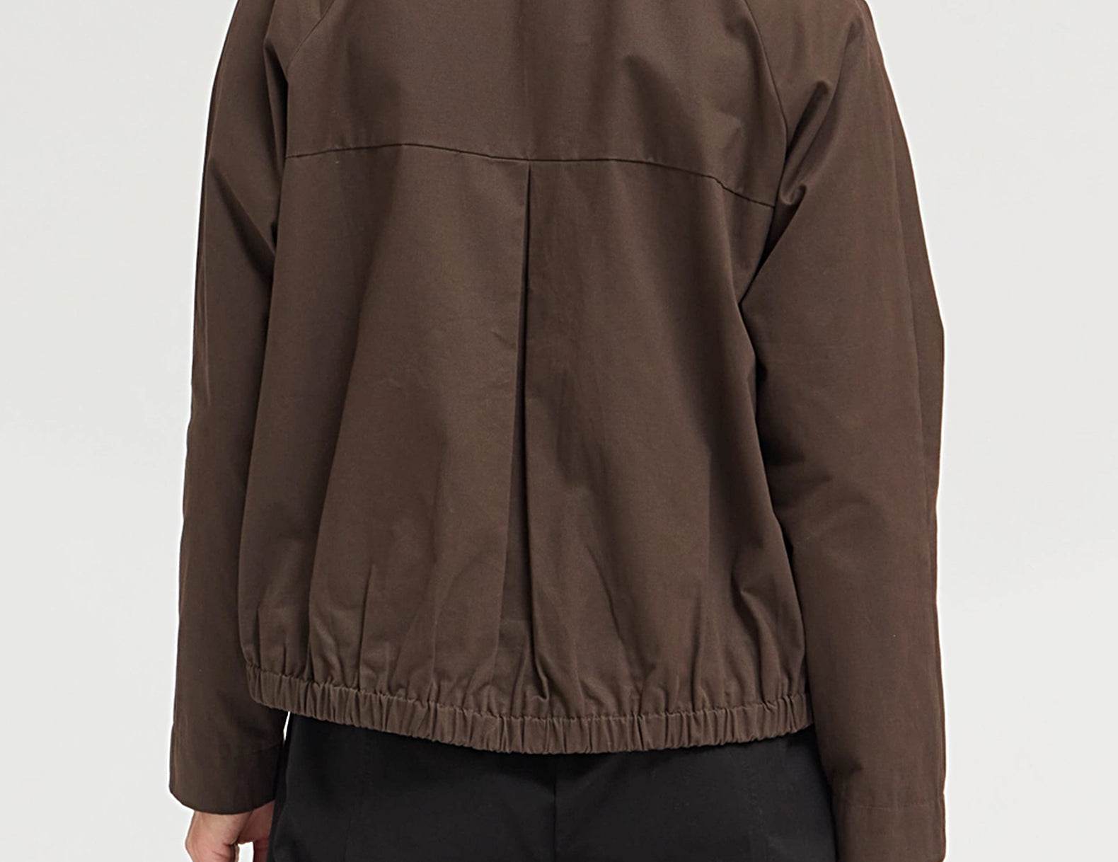 A person shown from the back wearing a dark brown lightweight jacket with a gathered elastic hem and black trousers, photographed against a plain light gray studio background.