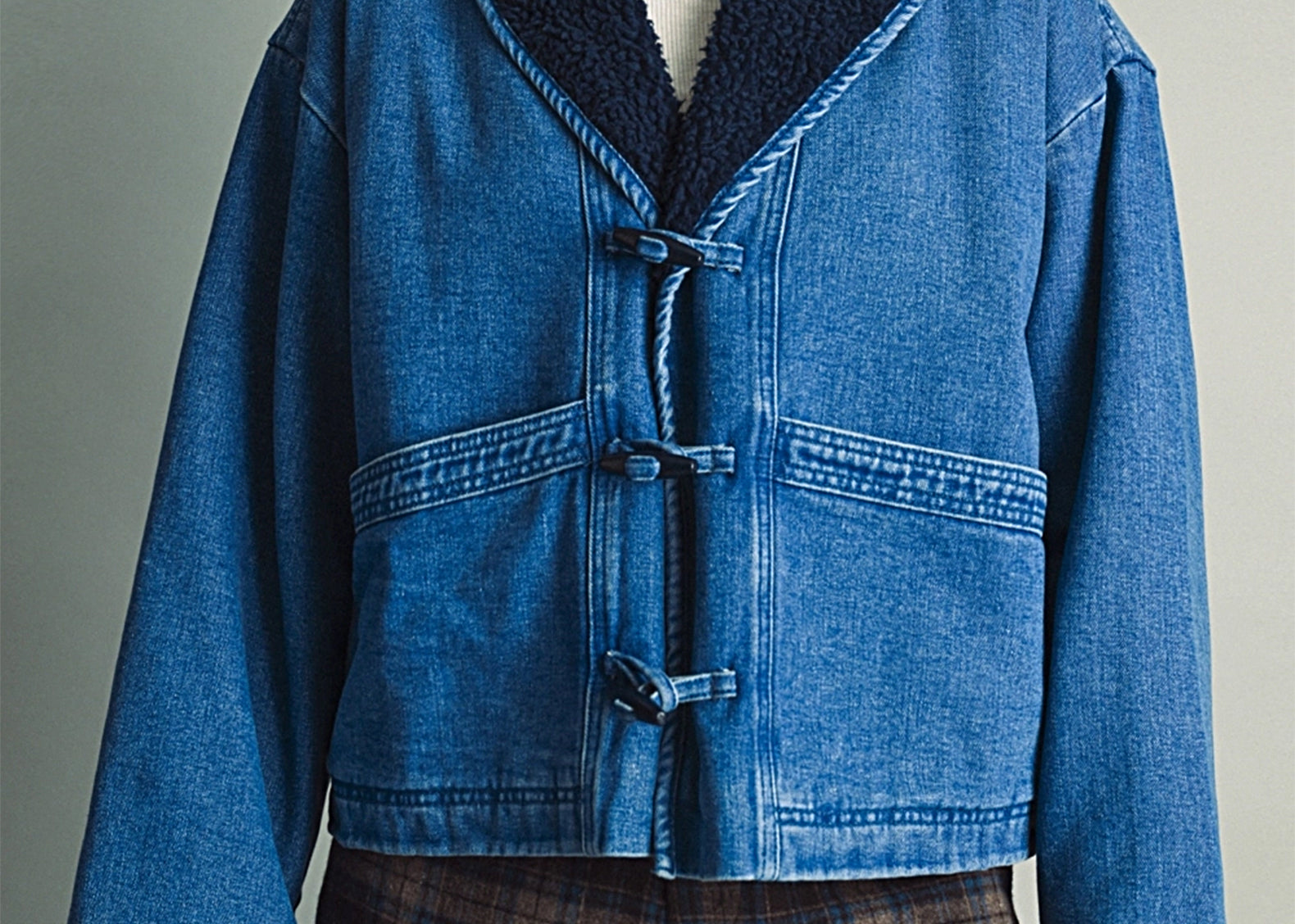 Front view of the Faye Toggle Button Sherpa + Denim Jacket, medium wash denim with a navy sherpa shawl collar, worn over a white turtleneck