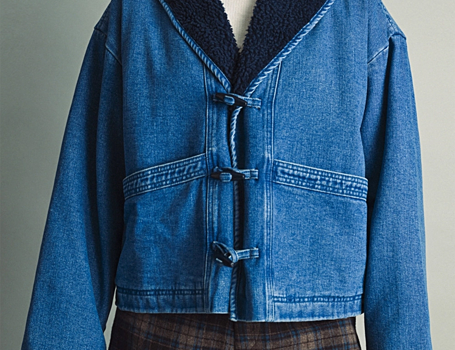 Front view of the Faye Toggle Button Sherpa + Denim Jacket, medium wash denim with a navy sherpa shawl collar, worn over a white turtleneck