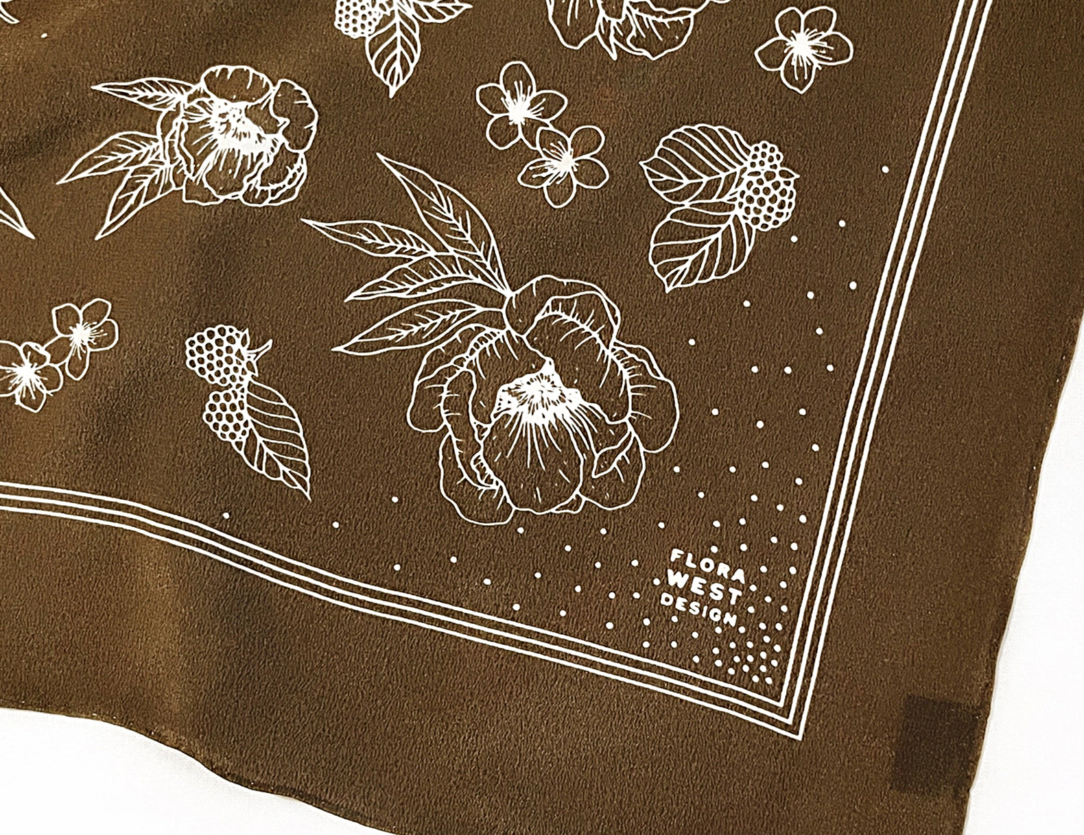 A brown silk scarf with a white floral and berry line-art pattern, featuring a white border and the text 'FASHION WEST DESIGN' printed in the lower right corner.