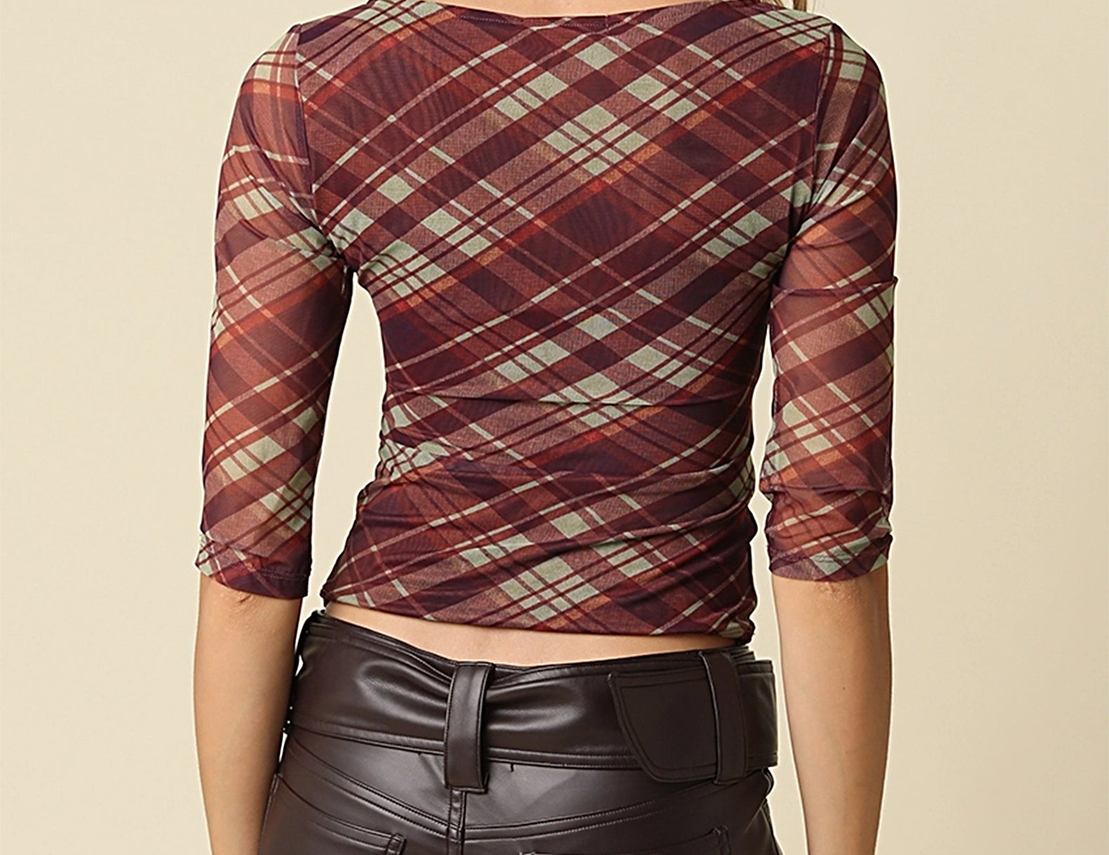 A woman shown from the back wearing a fitted three-quarter sleeve top with a burgundy, brown, and beige plaid pattern, paired with dark brown faux-leather pants, against a solid beige background.