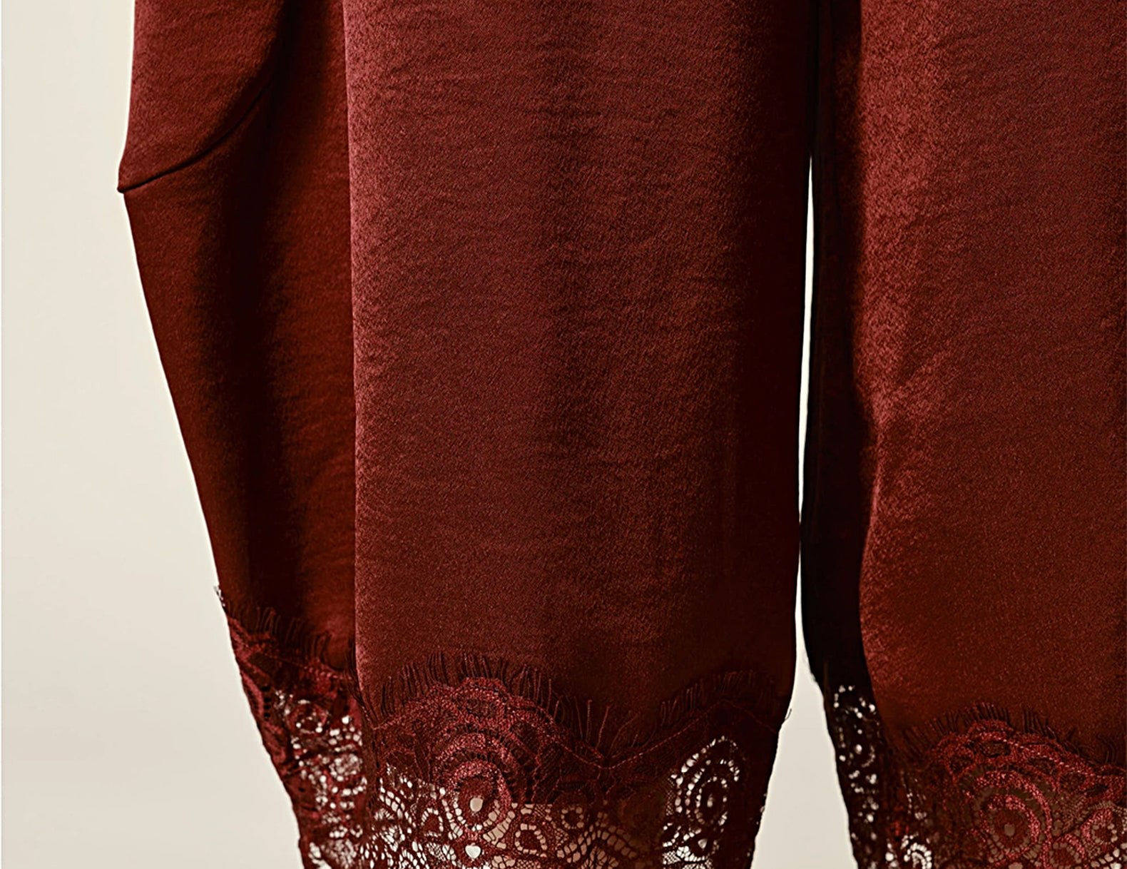 Close-up of a person wearing loose, wide-leg rust-brown satin harem pants with a decorative lace hem, paired with tan slip-on shoes against a plain light background.