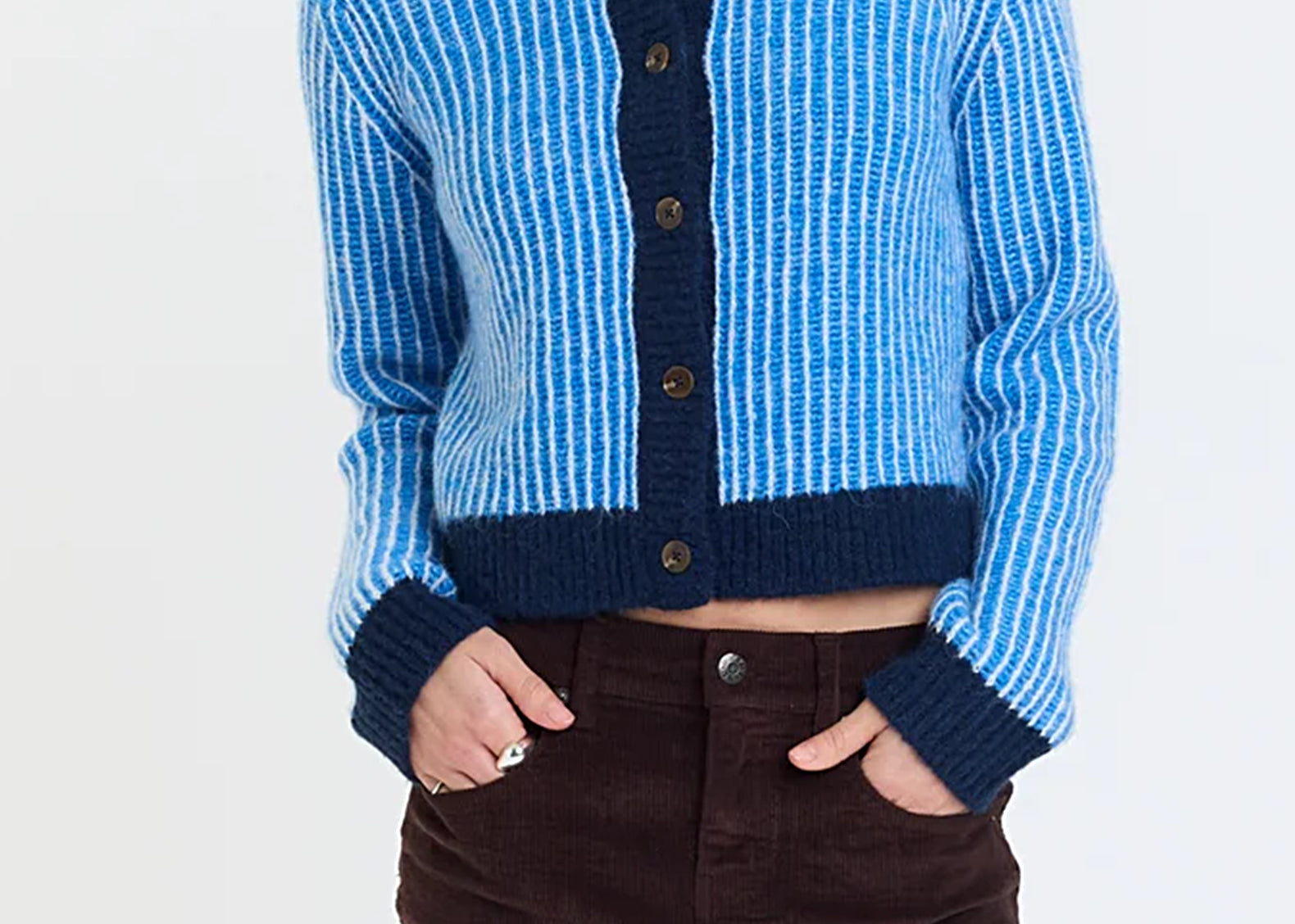 Front view of a cropped blue and white striped cardigan with navy trim, buttoned, worn with a high-rise mini skirt