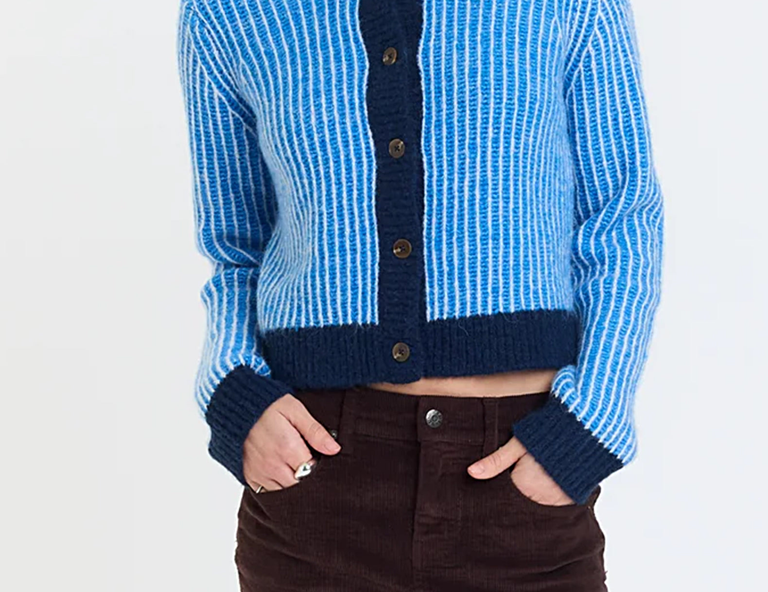 Front view of a cropped blue and white striped cardigan with navy trim, buttoned, worn with a high-rise mini skirt