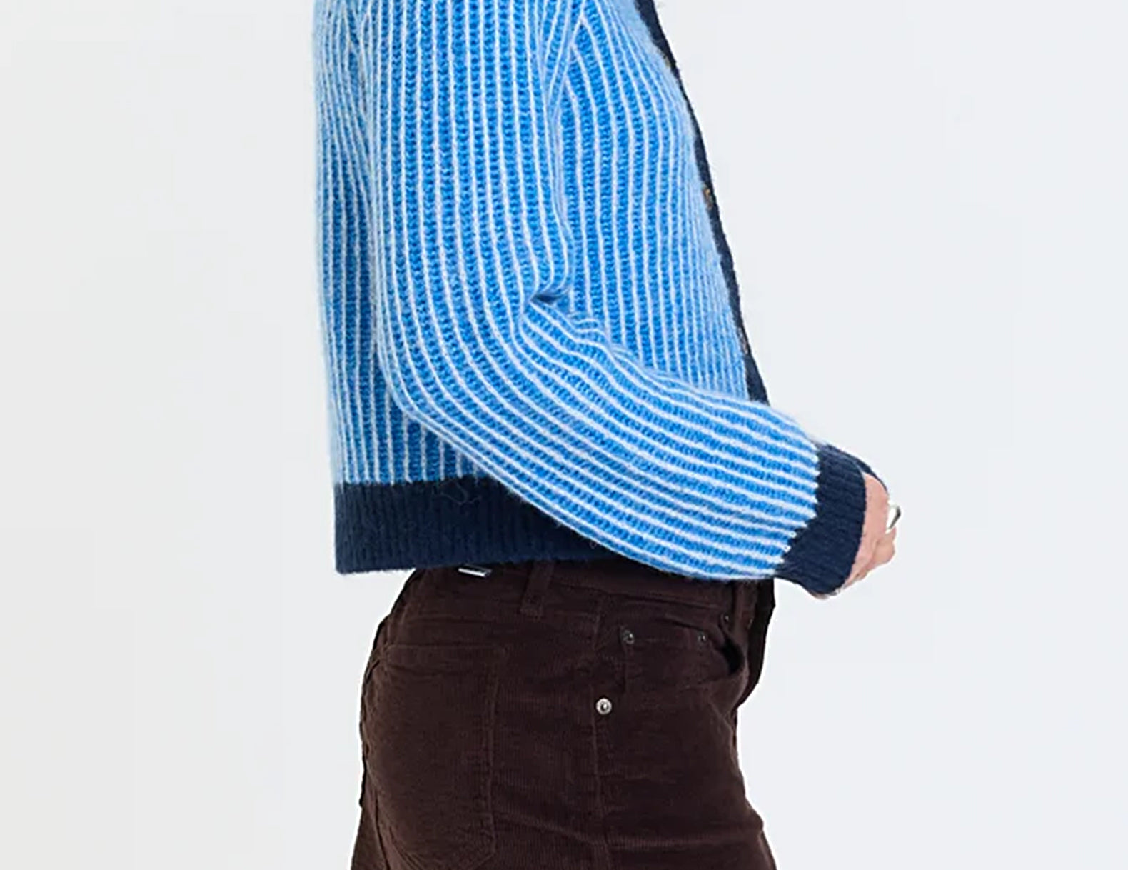 Side profile of a cropped blue knit cardigan showing the striped sleeve and navy cuff detail