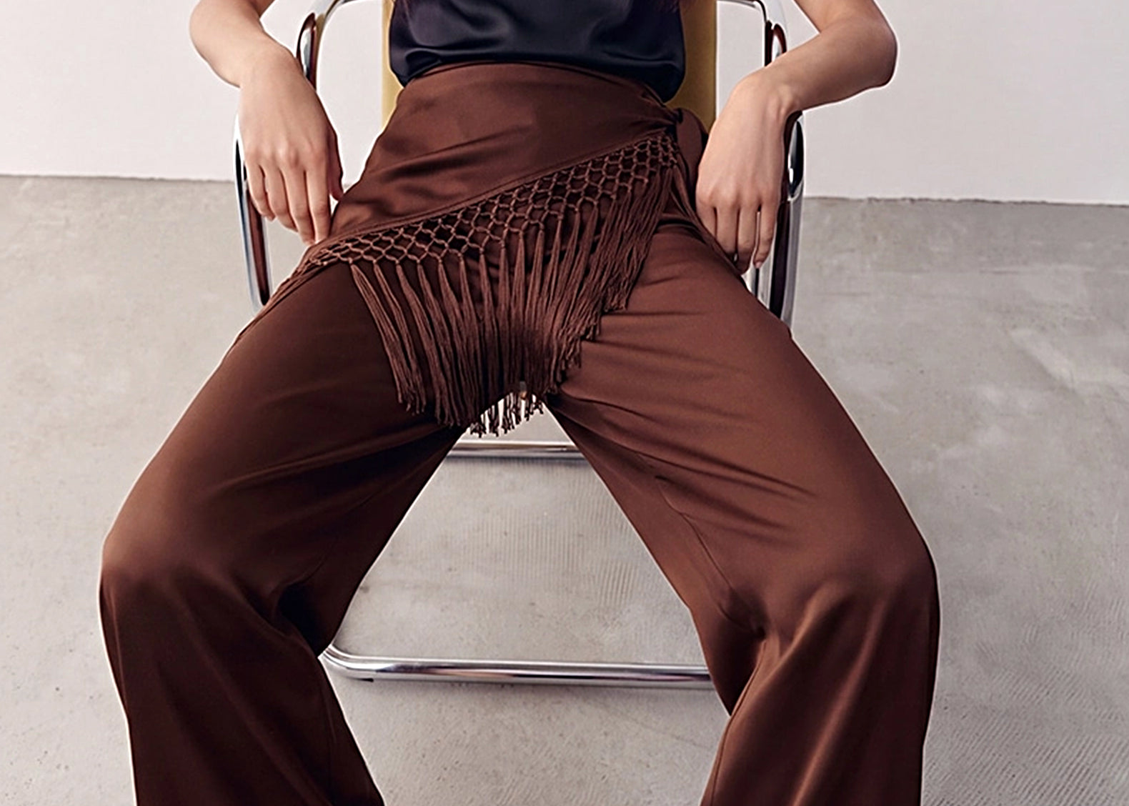 Chocolate Odette satin wide-leg pants with fringe scarf tied at the hip, styled seated 