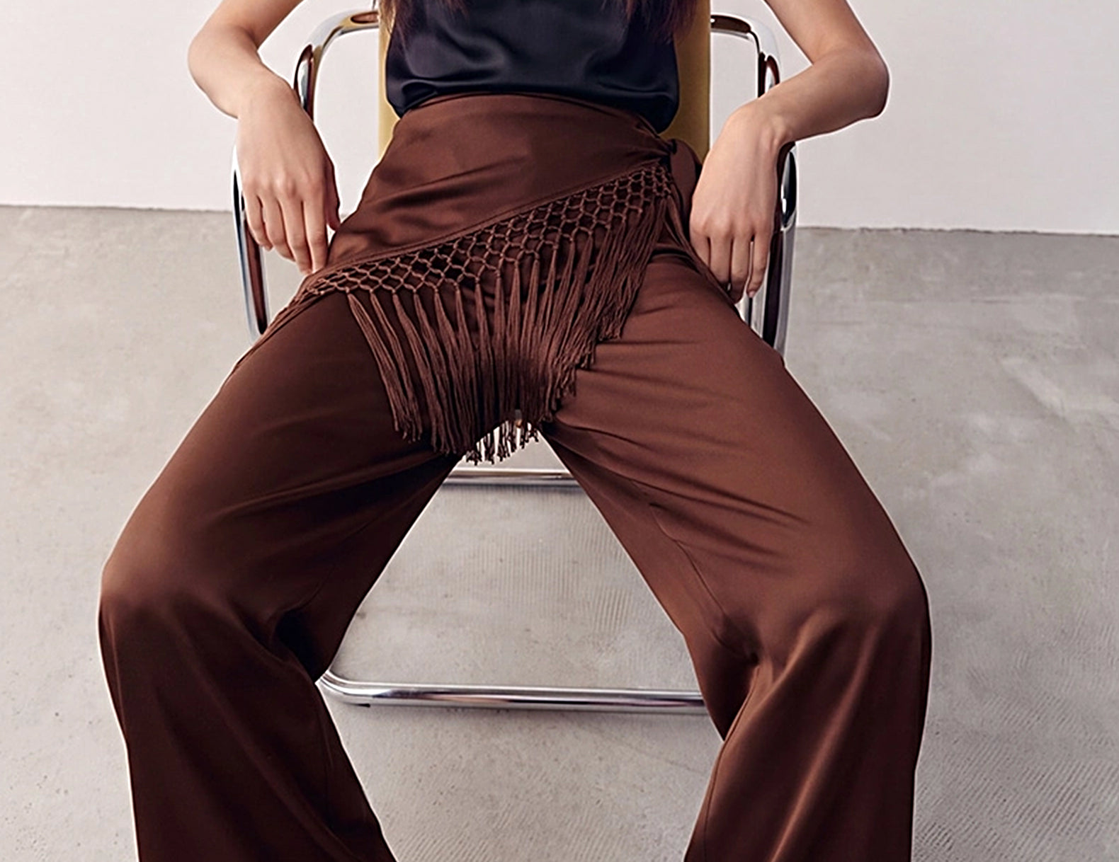 Chocolate Odette satin wide-leg pants with fringe scarf tied at the hip, styled seated 