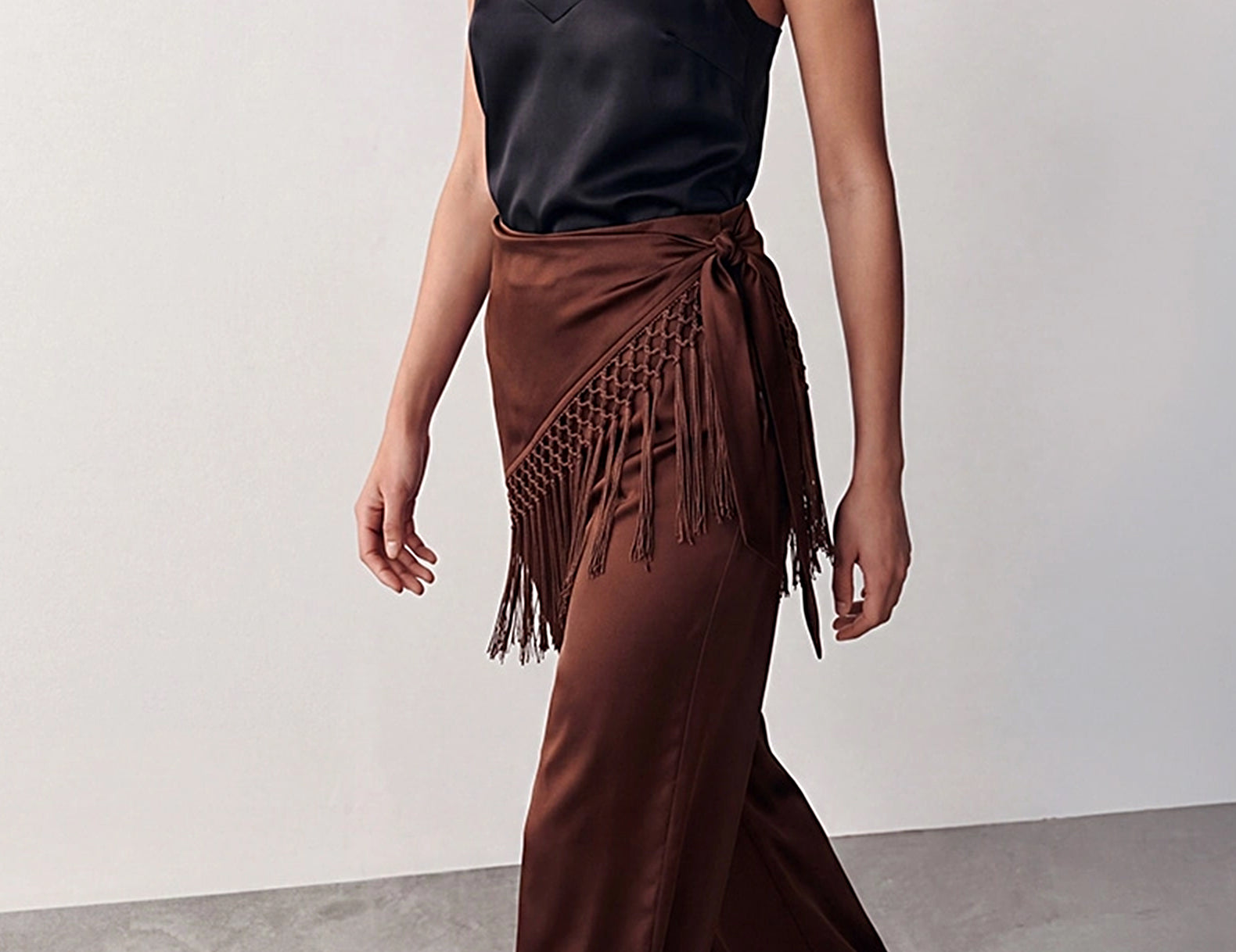 hree-quarter walking view of the chocolate satin pants with fringe scarf tied at the side