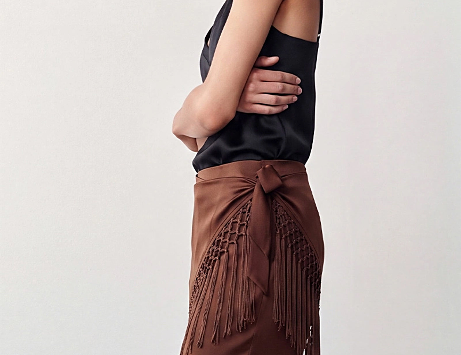 Side view of the chocolate fringe scarf knotted at the hip over satin pants

