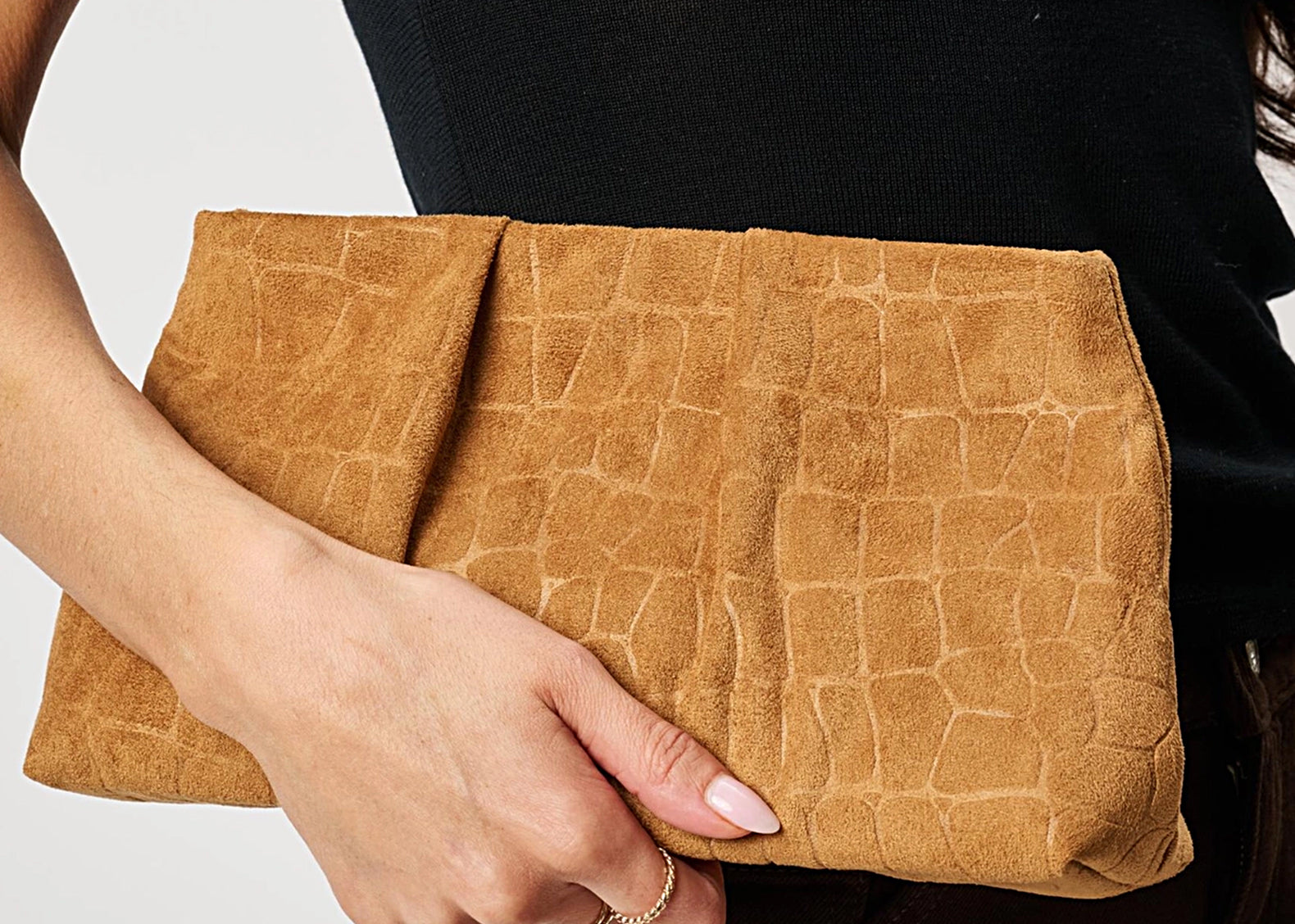 A person holding a tan faux-crocodile leather clutch bag against a light gray background.