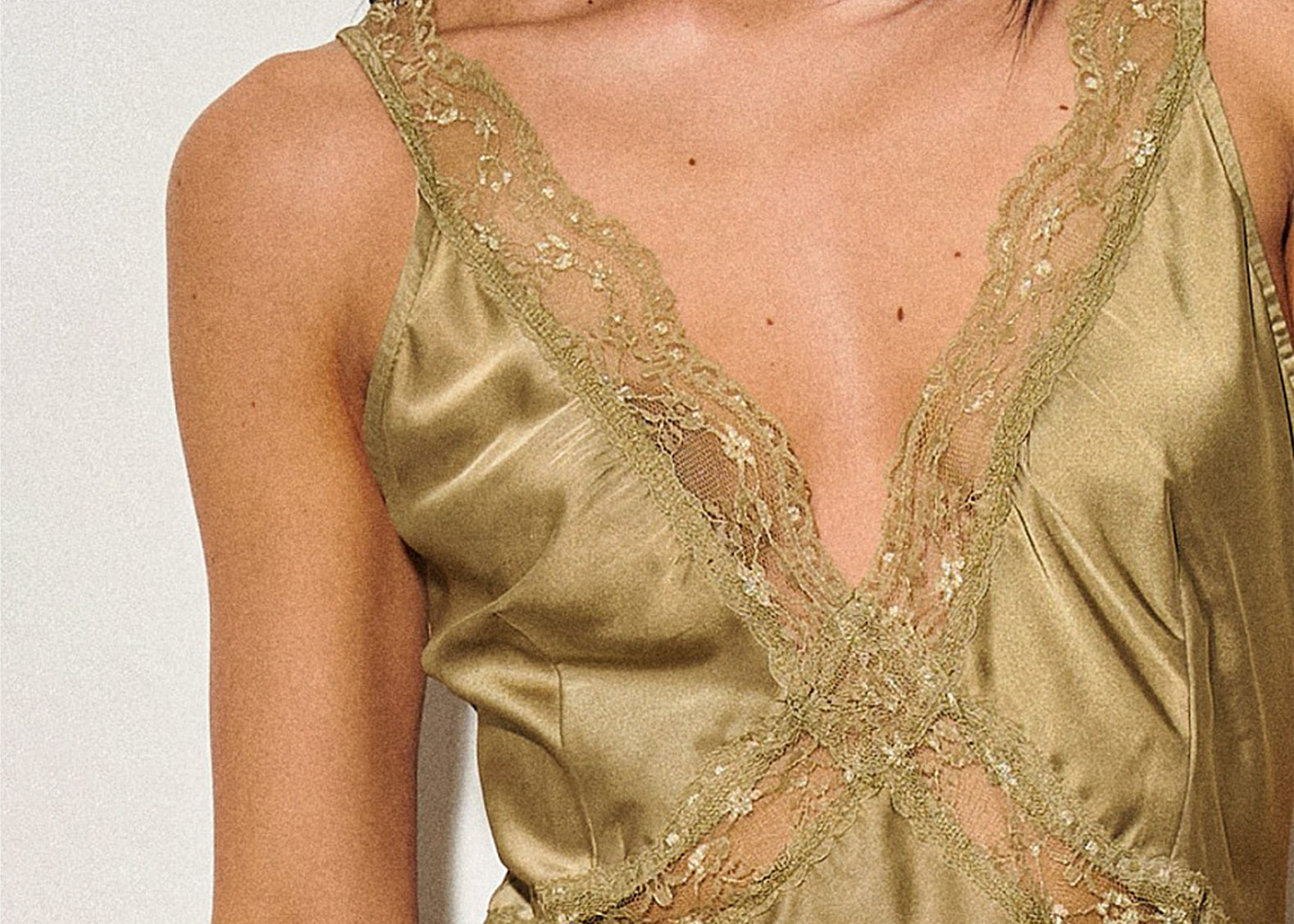Close-up of a model wearing a champagne gold satin camisole with intricate lace and embroidery details.