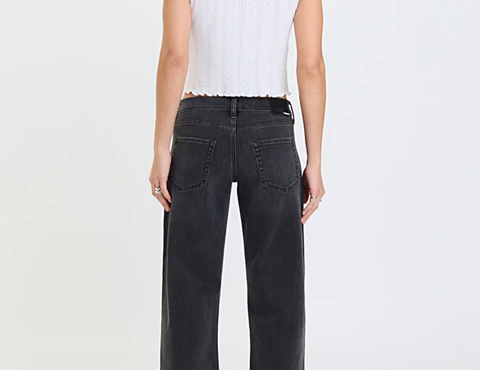A model shown from the back wearing a white ribbed short-sleeve crop top and dark gray wide-leg jeans against a plain white studio background.
