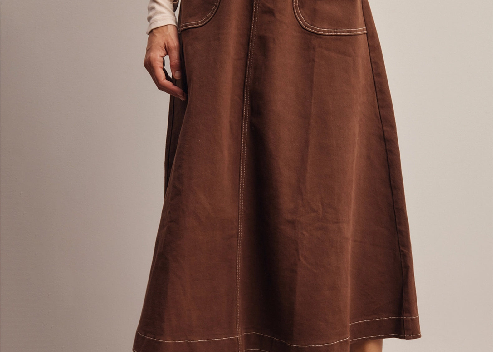Front view of the Shilo Chocolate Utility Pocket Midi Skirt with a hand in the front utility pocket, showing the cream contrast stitching