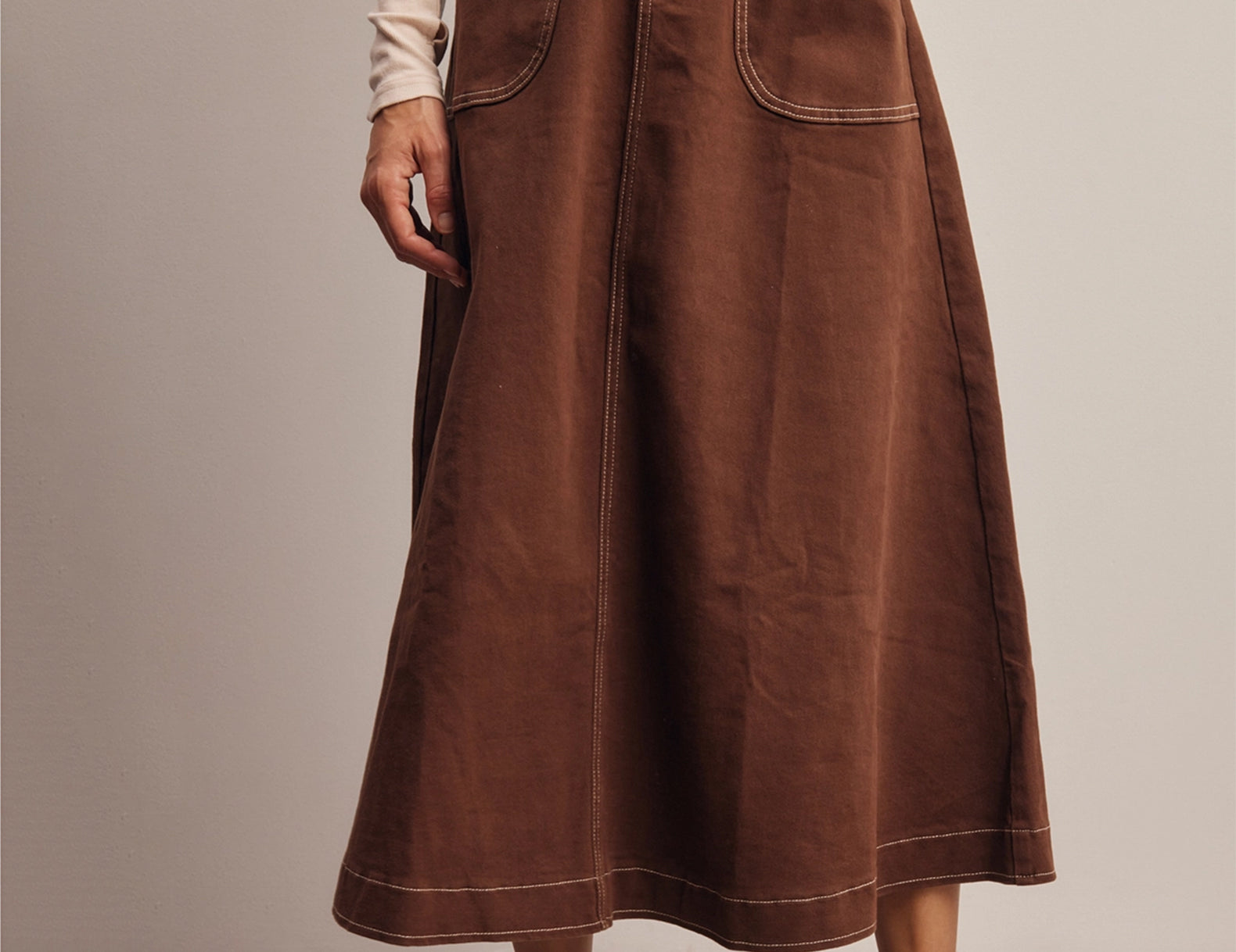 Front view of the Shilo Chocolate Utility Pocket Midi Skirt with a hand in the front utility pocket, showing the cream contrast stitching