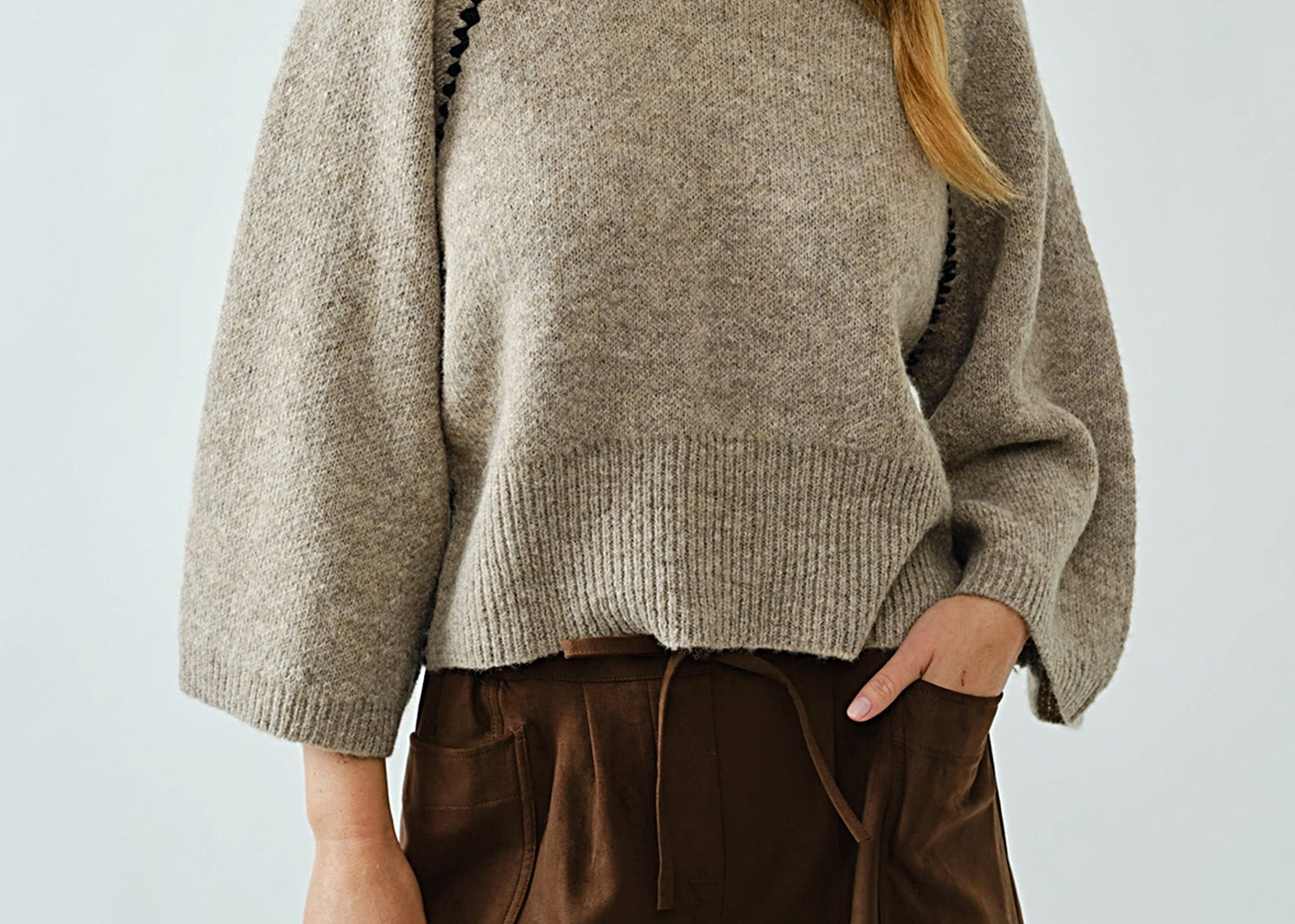 Woman wearing oatmeal raglan sweater with black whipstitch trim and brown shorts