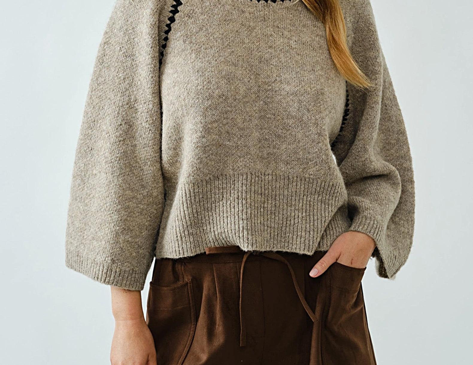 Woman wearing oatmeal raglan sweater with black whipstitch trim and brown shorts