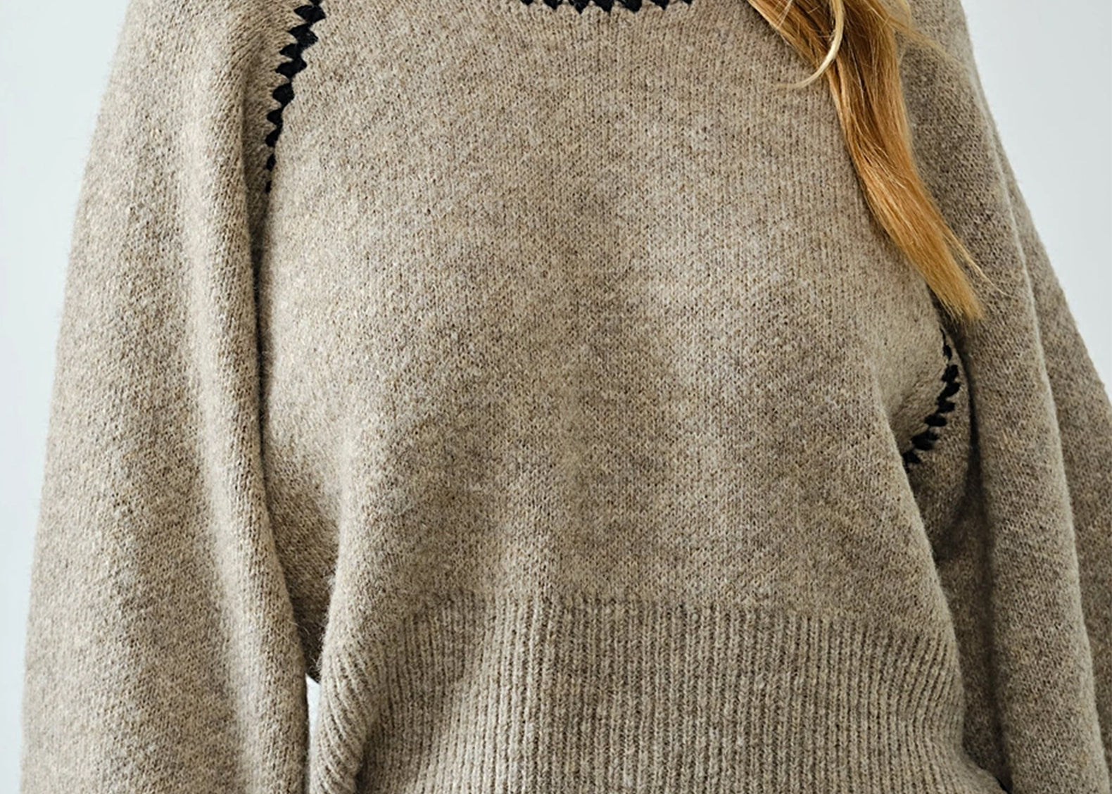 Close-up of black whipstitch detail on oatmeal knit sweater neckline
