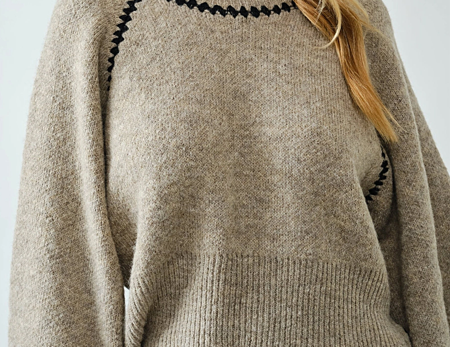 Close-up of black whipstitch detail on oatmeal knit sweater neckline